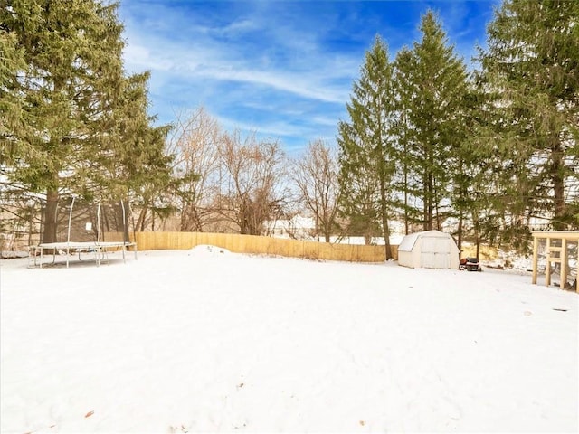 yard covered in snow featuring a trampoline and a storage shed