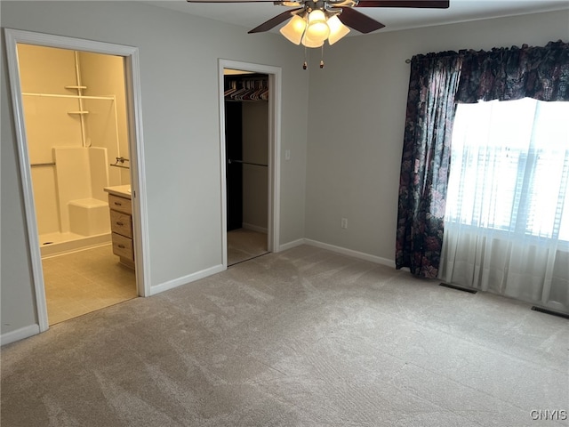 unfurnished bedroom featuring ceiling fan, connected bathroom, a walk in closet, light colored carpet, and a closet