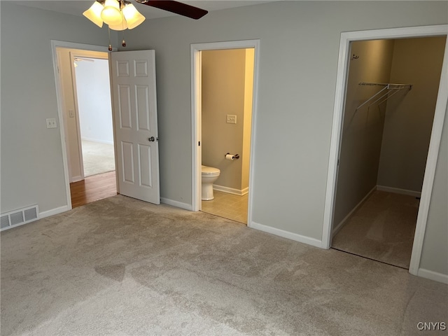 unfurnished bedroom featuring ensuite bath, ceiling fan, a walk in closet, light colored carpet, and a closet