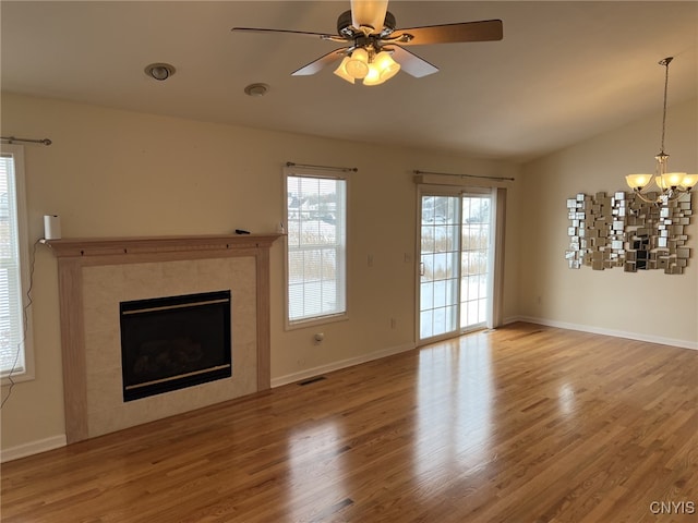 unfurnished living room with ceiling fan with notable chandelier, wood-type flooring, a fireplace, and vaulted ceiling