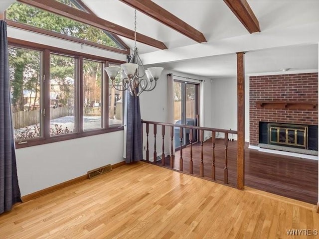 unfurnished dining area featuring a brick fireplace, a wealth of natural light, hardwood / wood-style floors, and beamed ceiling