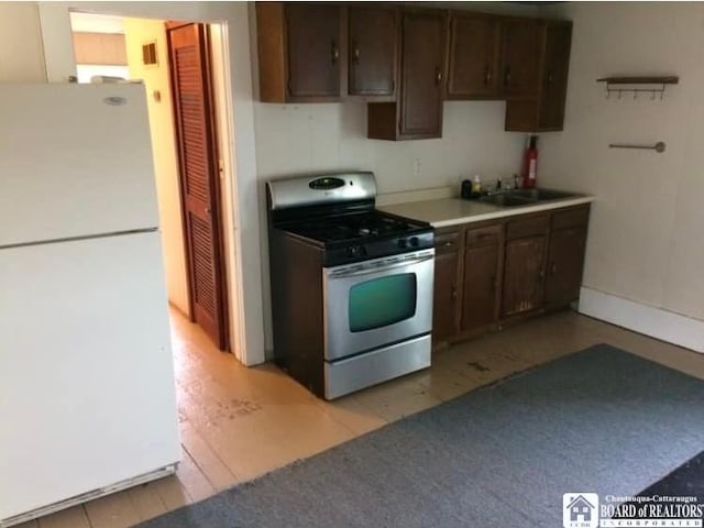 kitchen with dark brown cabinetry, sink, gas range, and white fridge