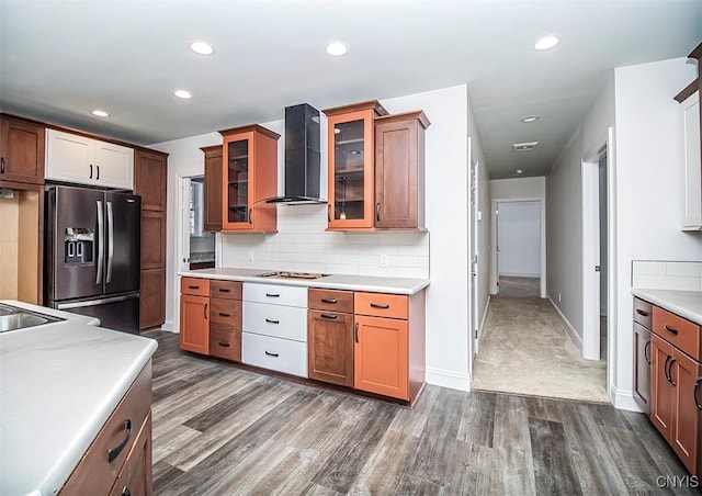 kitchen featuring wall chimney range hood, gas cooktop, backsplash, stainless steel refrigerator with ice dispenser, and dark hardwood / wood-style flooring