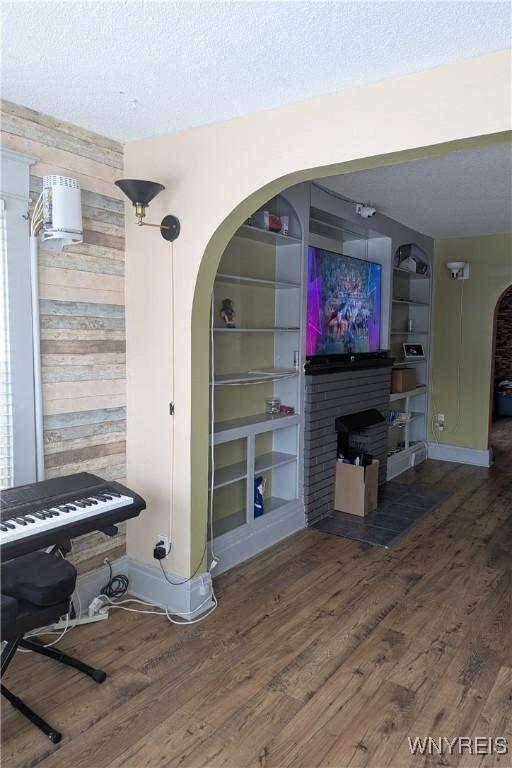 interior space featuring wooden walls, built in shelves, wood finished floors, a fireplace, and a textured ceiling