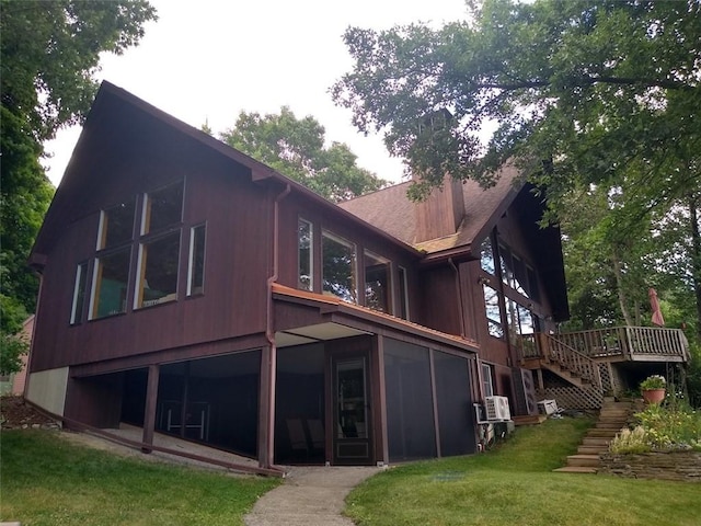 rear view of property featuring a sunroom, a deck, and a lawn