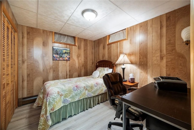 bedroom with wooden walls, light hardwood / wood-style floors, and baseboard heating