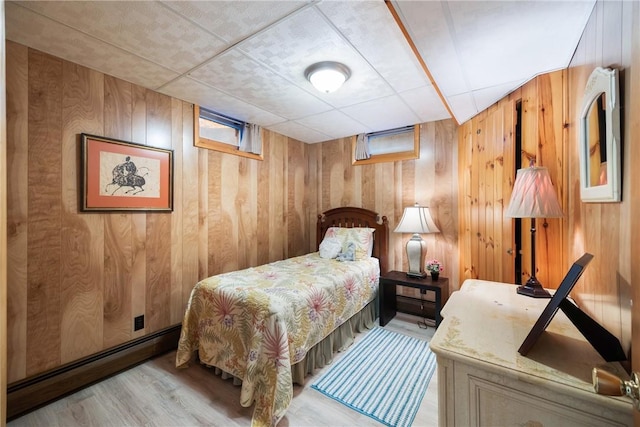 bedroom featuring light wood-type flooring, a baseboard heating unit, wooden walls, and a paneled ceiling