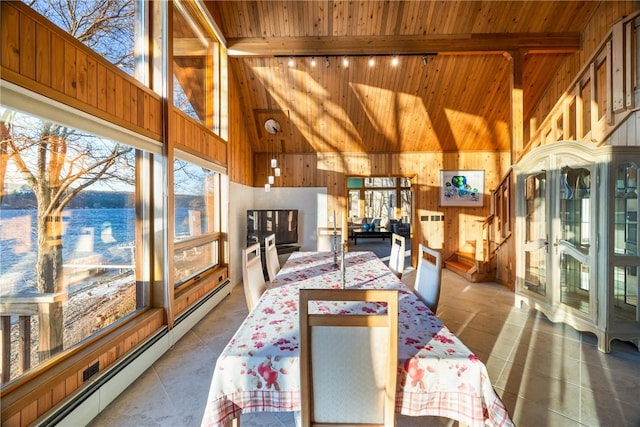 tiled dining room with rail lighting, a baseboard heating unit, beam ceiling, a towering ceiling, and wood walls