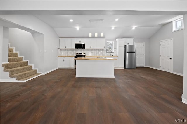 kitchen with lofted ceiling, a center island, appliances with stainless steel finishes, decorative backsplash, and white cabinets