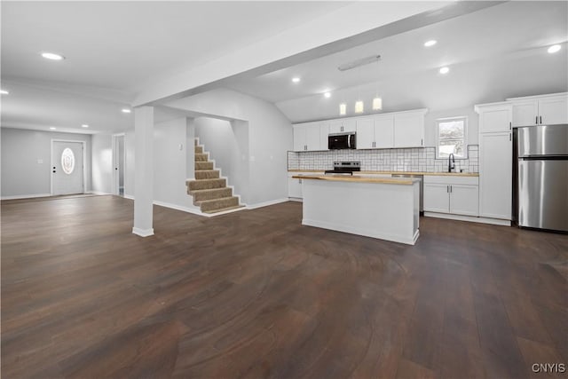 kitchen with butcher block countertops, sink, appliances with stainless steel finishes, white cabinets, and vaulted ceiling