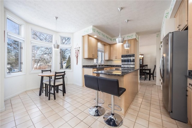 kitchen with a kitchen island, appliances with stainless steel finishes, light brown cabinetry, hanging light fixtures, and a textured ceiling