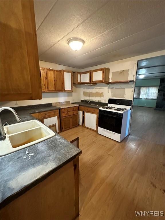 kitchen with wood-type flooring, sink, a textured ceiling, and gas range gas stove