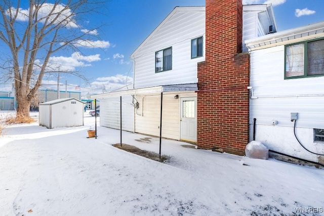 snow covered rear of property featuring a shed