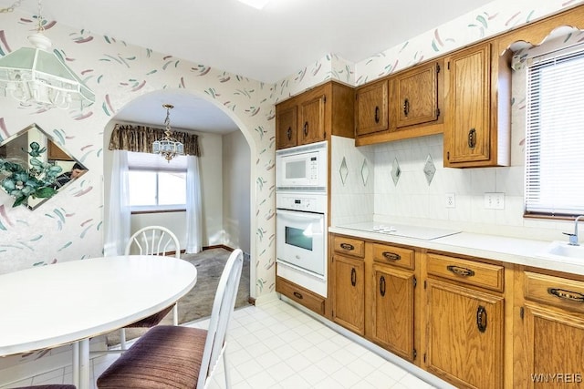 kitchen featuring sink, decorative backsplash, hanging light fixtures, white appliances, and an inviting chandelier