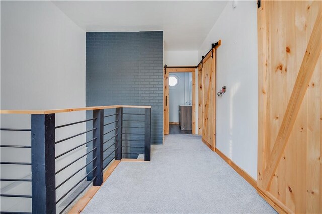 hallway featuring carpet flooring, an upstairs landing, baseboards, and a barn door