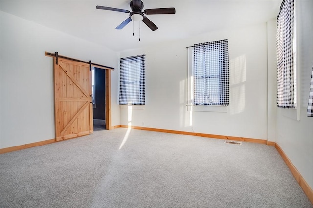 unfurnished bedroom featuring a barn door, carpet flooring, and ceiling fan