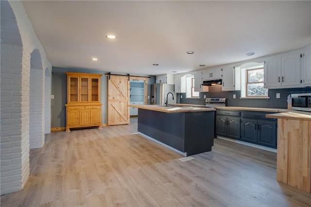 kitchen with white cabinets, stainless steel appliances, a barn door, and light wood-type flooring