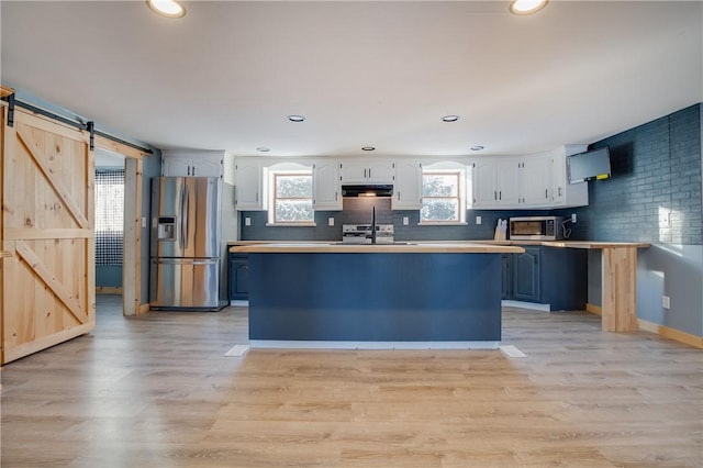 kitchen featuring stainless steel appliances, a barn door, white cabinetry, light wood-style floors, and extractor fan