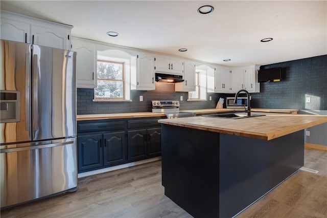kitchen with range hood, a sink, wood counters, light wood-style floors, and appliances with stainless steel finishes