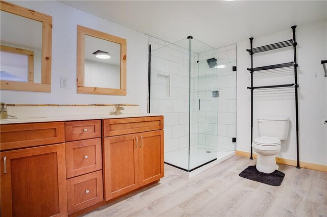 full bathroom featuring double vanity, a tile shower, toilet, wood finished floors, and a sink