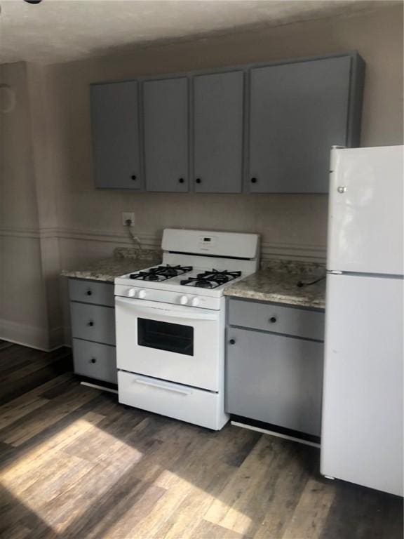 kitchen featuring light stone countertops, dark hardwood / wood-style floors, gray cabinetry, and white appliances