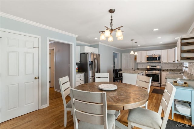 dining space with sink, a notable chandelier, ornamental molding, and light hardwood / wood-style floors