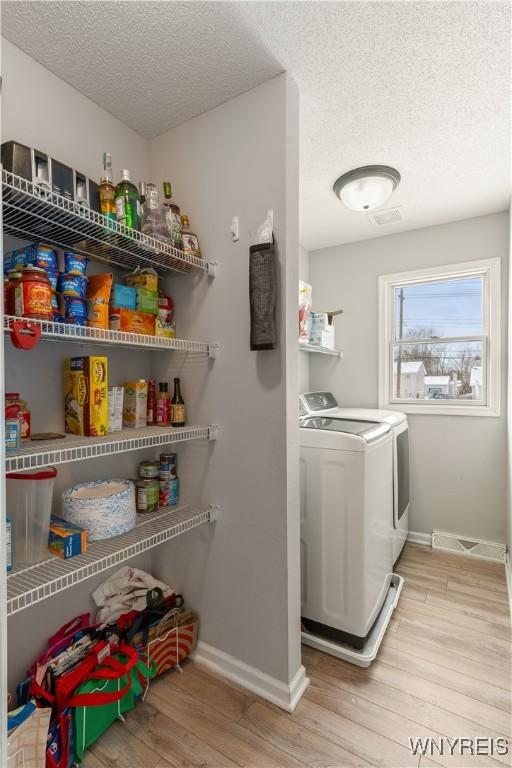 laundry area featuring washing machine and dryer, a textured ceiling, and light hardwood / wood-style floors