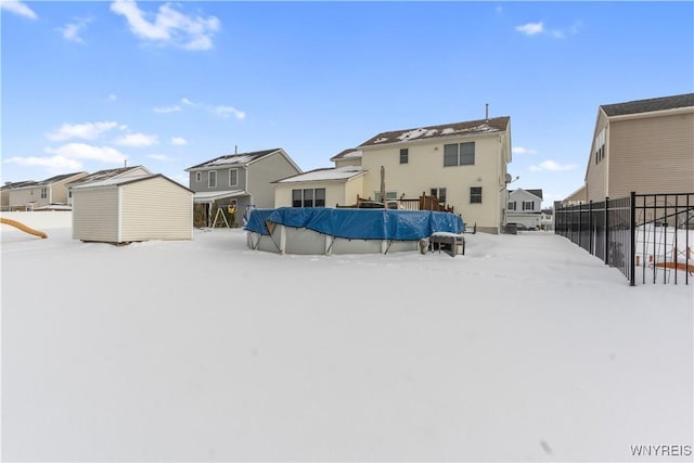 snow covered back of property featuring a covered pool and a shed