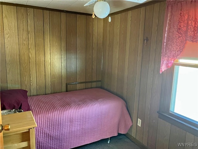 carpeted bedroom featuring ceiling fan and wood walls