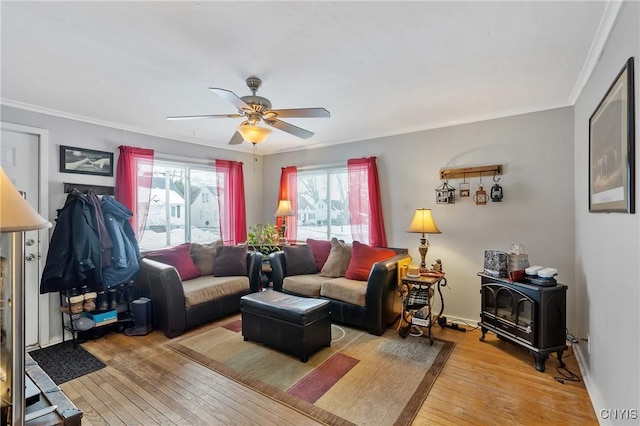 living room with crown molding, ceiling fan, wood-type flooring, and a wood stove