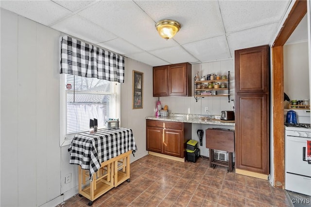 kitchen with a paneled ceiling, white gas range oven, and wood walls