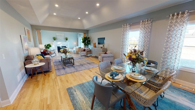 dining space featuring decorative columns, light hardwood / wood-style flooring, and a tray ceiling