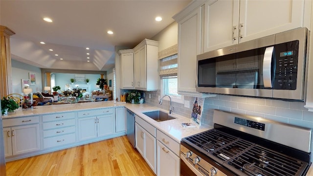 kitchen featuring sink, white cabinetry, stainless steel appliances, light hardwood / wood-style floors, and backsplash