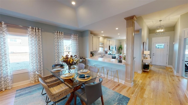 dining space with sink, a notable chandelier, ornate columns, and light wood-type flooring