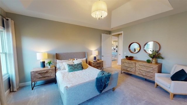 carpeted bedroom featuring ensuite bath, a raised ceiling, and a chandelier