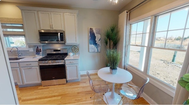 kitchen featuring tasteful backsplash, sink, white cabinets, stainless steel appliances, and light hardwood / wood-style flooring