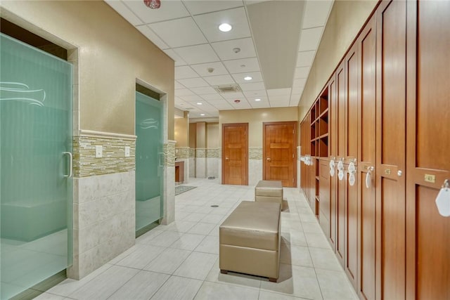 hallway with a paneled ceiling, tile walls, and light tile patterned floors