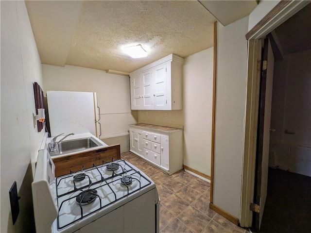 kitchen featuring white gas range, sink, white cabinets, and a textured ceiling