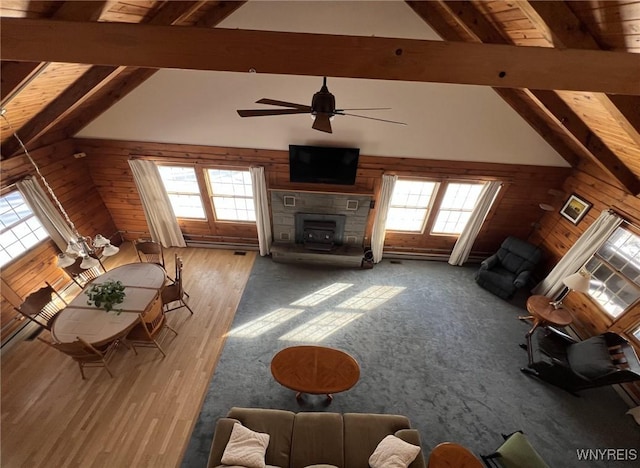 unfurnished living room with a stone fireplace, lofted ceiling with beams, ceiling fan, and wood walls