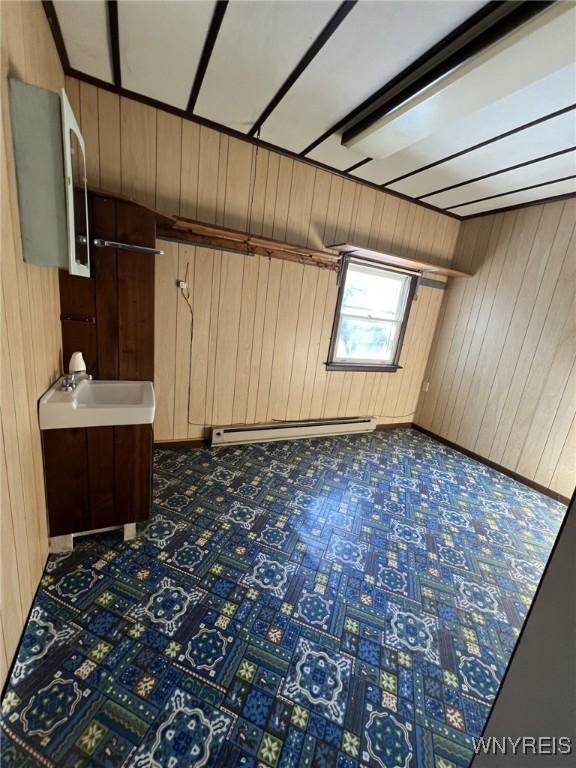 spare room with a baseboard heating unit, a sink, and wooden walls