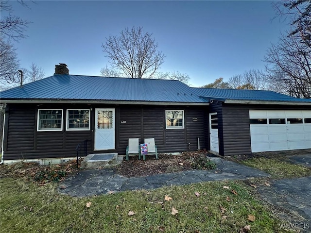 ranch-style home with a garage, faux log siding, metal roof, and a chimney