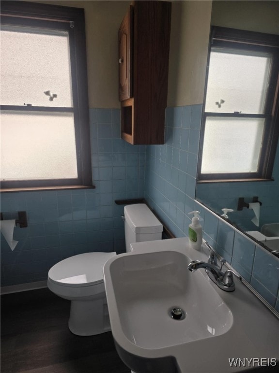 bathroom featuring wood-type flooring, toilet, sink, and tile walls