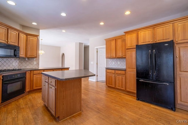 kitchen featuring backsplash, light hardwood / wood-style floors, a kitchen island, and black appliances