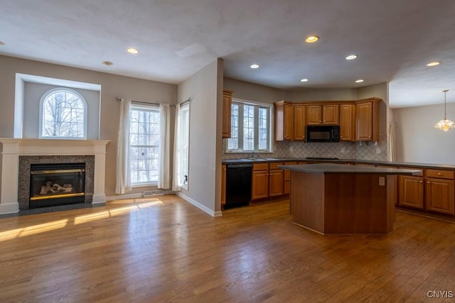 kitchen with a center island, light wood-type flooring, pendant lighting, decorative backsplash, and black appliances