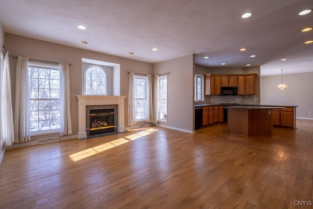 kitchen with a kitchen island, pendant lighting, backsplash, light hardwood / wood-style floors, and black appliances