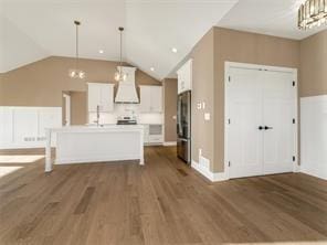 kitchen with stainless steel refrigerator, decorative light fixtures, white cabinets, custom range hood, and a center island with sink