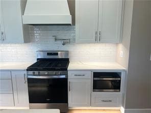 kitchen featuring tasteful backsplash, white cabinetry, stainless steel range with gas stovetop, and custom exhaust hood