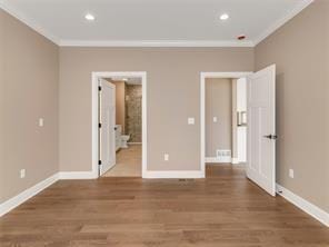 unfurnished bedroom featuring hardwood / wood-style floors, ornamental molding, and ensuite bathroom