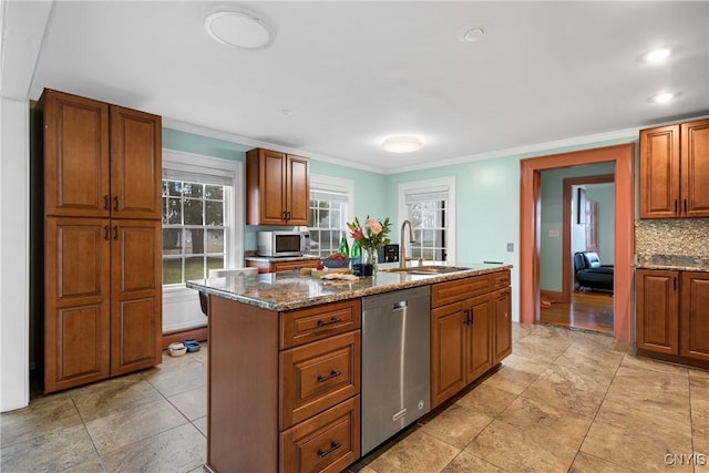 kitchen featuring sink, dark stone countertops, stainless steel appliances, ornamental molding, and an island with sink