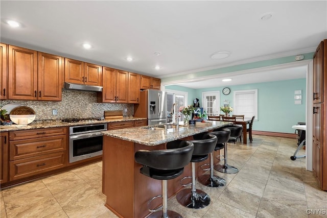 kitchen featuring a breakfast bar, sink, stainless steel appliances, light stone countertops, and a kitchen island with sink